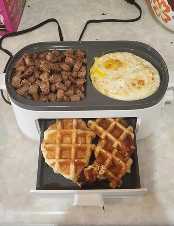 Cooked steak cubes, a fried egg, and a waffle on a divided electric grill.