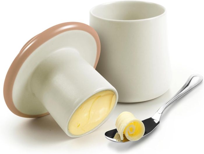 Butter stored in a mushroom-shaped ramekin with a lid, next to a curl of butter on a spoon