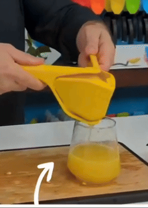 A person pressing down on a hand-held juicer, squeezing juice into a glass.