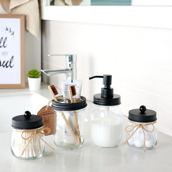 The four mason jars with black lids, including a soap dispenser, a jar with two toothbrushes, and two smaller jars holding cotton balls and swabs with easy-to-lift tops.