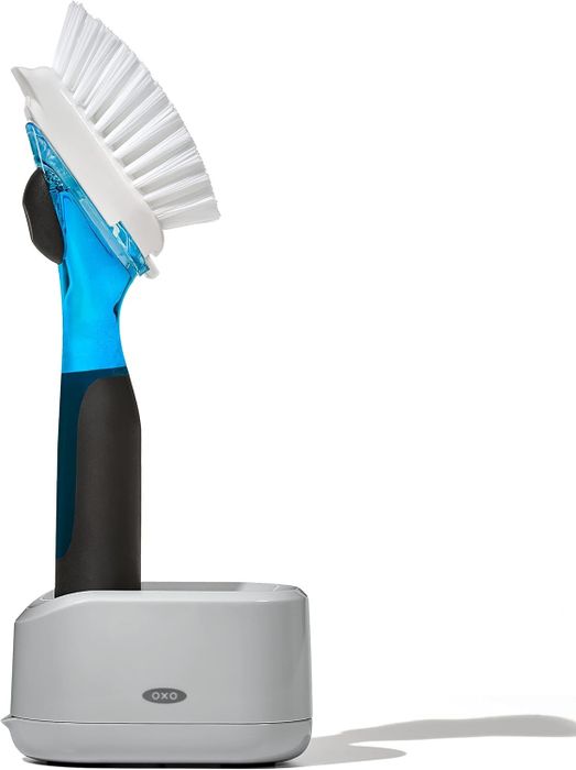 A brush with an ergonomic handle that holds soap inside and sits in a stand