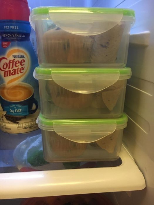 Three plastic containers stacked in a fridge, each containing muffins, with Coffee-mate creamer and other grocery items beside them