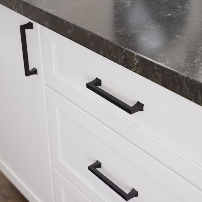 A close-up image of a kitchen countertop featuring black handles on white cabinet drawers below. The surface of the countertop is smooth and dark, creating a modern and sleek look.