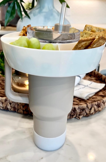 A small white plastic bowl with a hole in it resting around the lid of a handled Stanley cup water tumbler