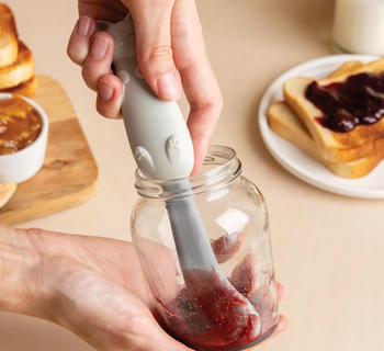 A hand using a cat-shaped spatula to scoop jelly out of a jar