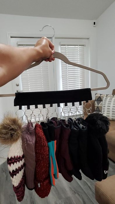 A hand holding a hanger with several winter hats and gloves attached, demonstrating a smart solution for organizing accessories.