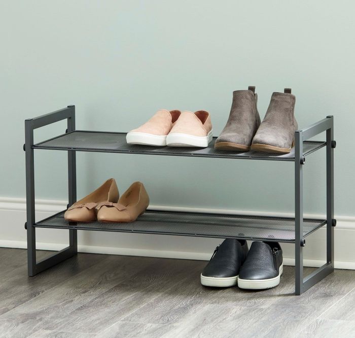 A two-tier metal shoe rack showcasing four pairs of shoes: pink slip-ons, brown boots, beige flats, and black sneakers