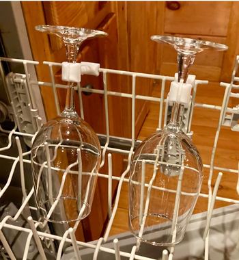 Two wine glasses placed upside-down in a dishwasher rack, held securely by white attachments.