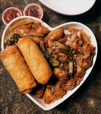 A heart-shaped plate filled with egg rolls and a chicken dish.