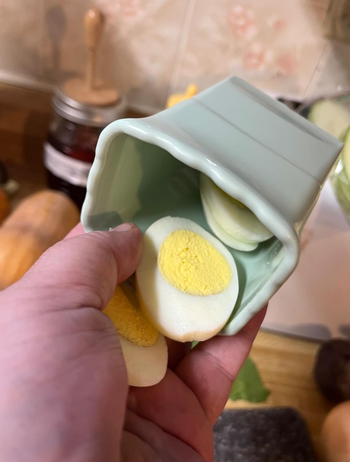 A hand holding a green cup with a hard-boiled egg sliced into several pieces