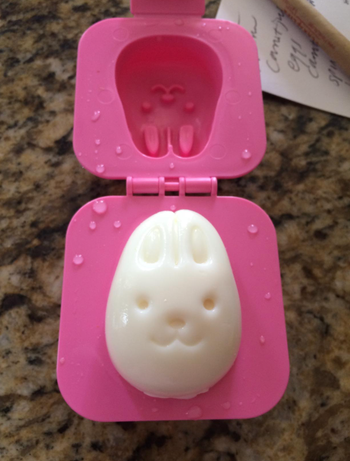 A hard-boiled egg molded into the shape of a bunny’s face, inside a pink mold with the lid open