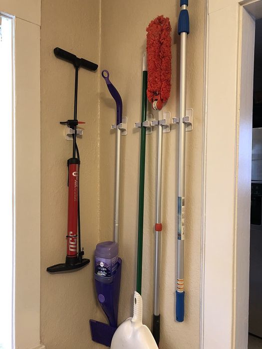 A photo shows the individual clips arranged on a wall, holding a broom, Swiffer, duster, and even a tire pump.