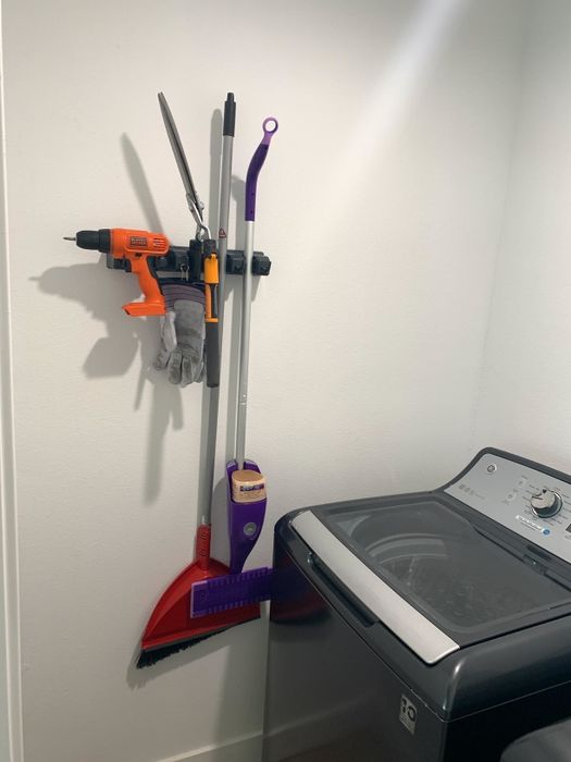 A reviewer shares a photo of their organizer, which holds a broom, Swiffer, and even a drill, all neatly hung.