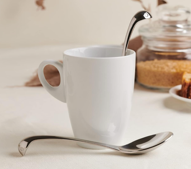 A silver spoon designed with a subtle Loch Ness monster figure peeking out from a mug