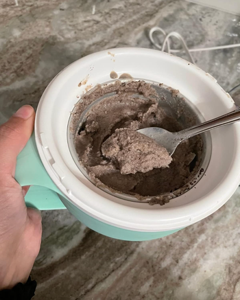 A person holding a cup with a spoon and ice cream inside.