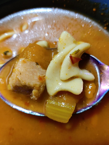 A close-up of traditional soup with meat, pasta, and vegetables in a bowl.