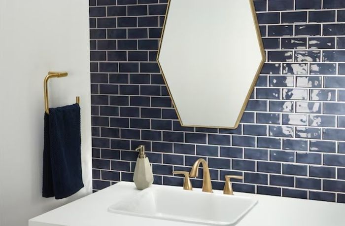 A contemporary bathroom sink accompanied by a gold-framed mirror, gold fixtures, navy blue tiled wall, and a navy towel hanging on a gold towel holder.