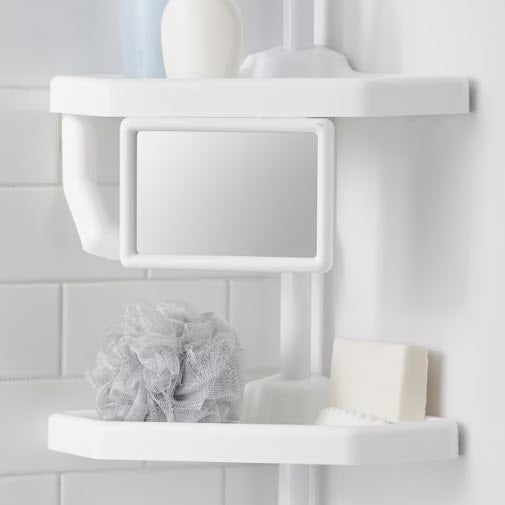 A white shower caddy mounted to the tiled wall of a bathroom, featuring a small mirror, a loofah, a bar of soap, and a toothbrush in a clean, minimalist setting.