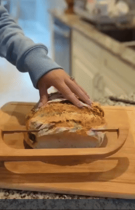 A person using a bow cutter knife to slice freshly baked bread.