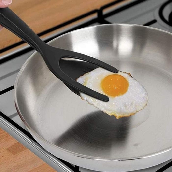 A single fried egg in a pan, being lifted by black tongs.