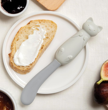A cat-shaped spatula spreading cream cheese on toast