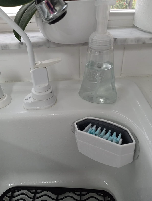 A double-sided bristled cutlery cleaner attached to the edge of a sink.