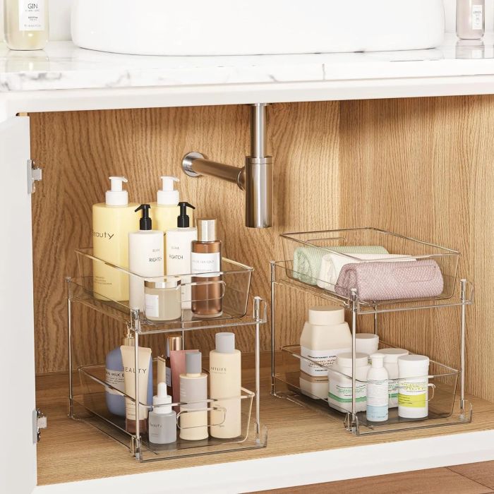 Neatly arranged under-sink storage featuring various beauty and skincare bottles, sorted on clear acrylic shelves. A folded towel is also visible.