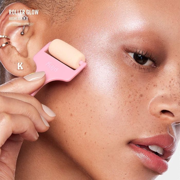 Model applying the highlighting roller to her cheekbone for a luminous finish.