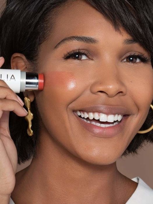 A model with a darker skin tone applying the multi-stick to her cheek.