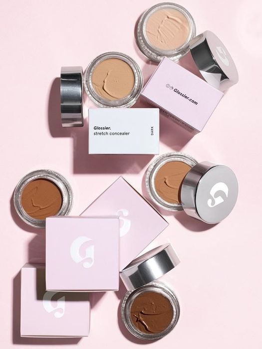 Various shades of the concealer displayed against a soft pink background.