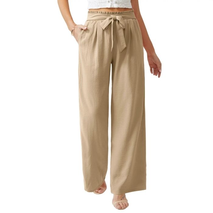 A model is dressed in beige wide-leg pants, cinched at the waist with a belt, and paired with nude heeled sandals for a relaxed yet sophisticated look.