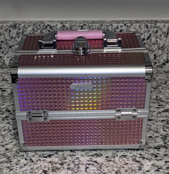 An iridescent pink travel case with a textured pattern and silver metal accents, resting on a granite counter.