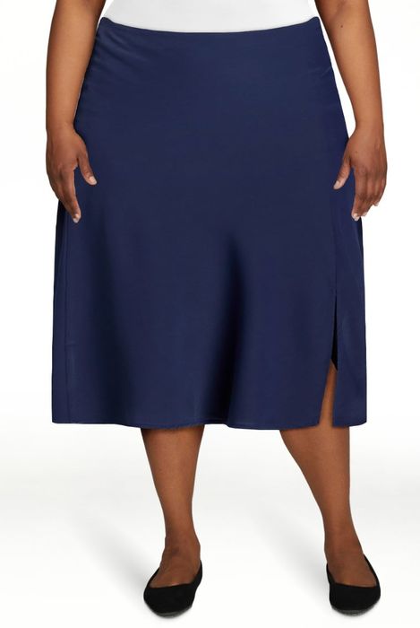 A person wearing a knee-length skirt with a side slit and flats, standing indoors