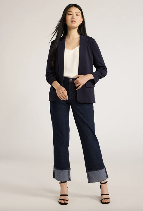 A woman in a fashionable blazer, white top, and wide-leg jeans, posing with confidence for a fashion feature.