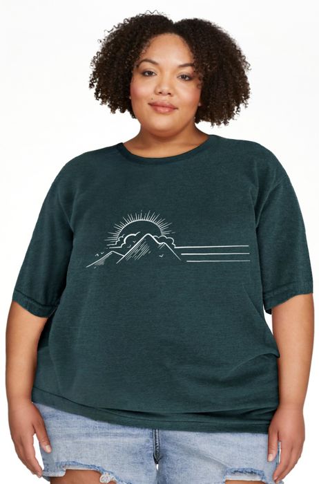 Person rocking a casual t-shirt featuring a mountain and sun graphic, paired with denim shorts