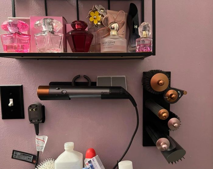 Perfume bottles and hair styling tools, including a Dyson Airwrap set, neatly arranged on a wall shelf