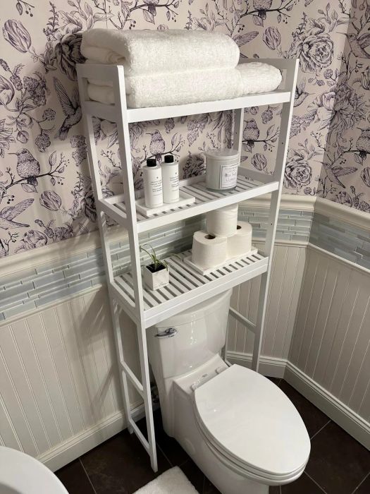 Bathroom shelving unit placed over the toilet, holding towels, toiletries, and toilet paper on its shelves