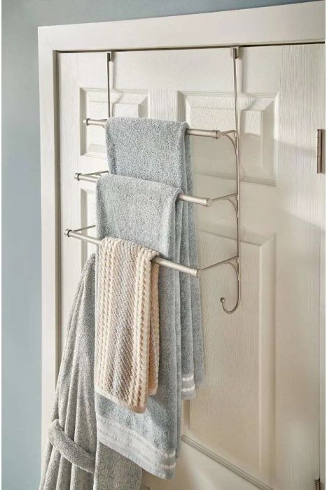 The back of a bathroom door featuring a towel rack with three tiers for hanging towels.