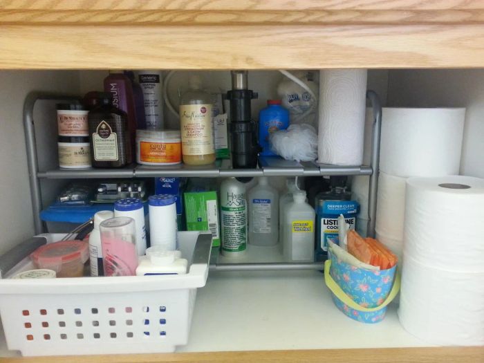 Bathroom cabinet stocked with an assortment of cleaning and personal care products, including paper towels, mouthwash, and toiletries
