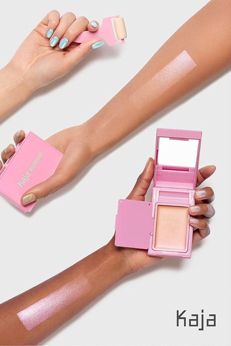 Three hands of varying skin tones holding the product, with swatches of the highlighter on their arms.
