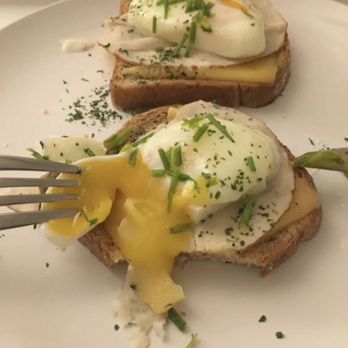 A reviewer using a fork to break into a poached egg placed on toast.
