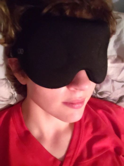 A reviewer wearing a sleek black sleep mask.