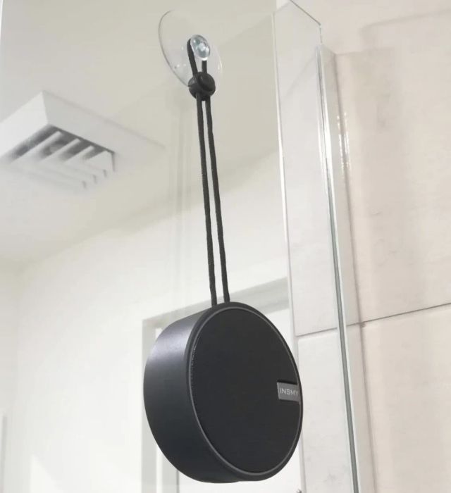 A reviewer shows the black Bluetooth shower speaker hanging from a suction cup inside the shower.