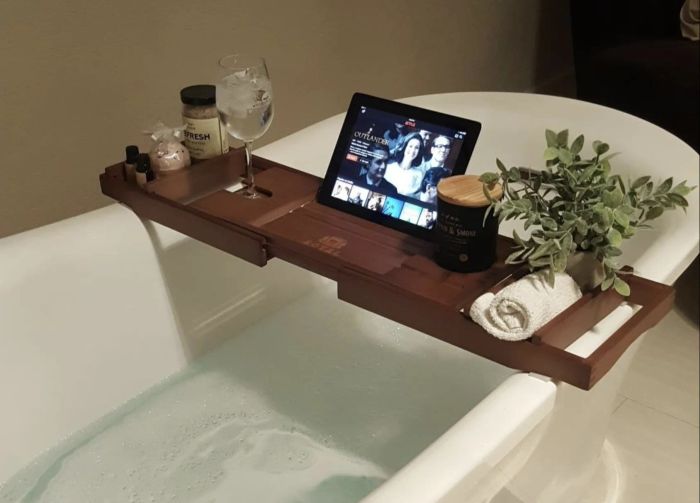 An image of a wooden bath caddy that holds an iPad, washcloth, plant, candle, wine glass, and bath salts.