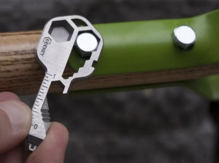 A compact steel tool designed in the shape of a key, featuring various grooves and measurements for practical use.