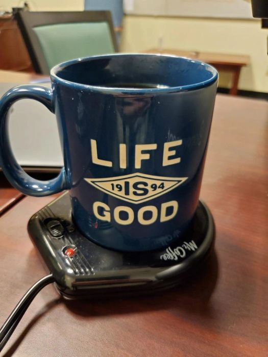 A steaming mug of coffee resting on a sleek black mug warmer pad.