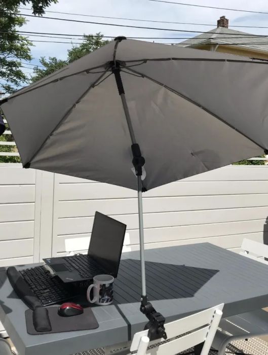 A white umbrella clamped to a chair, providing shade for a laptop on a table.