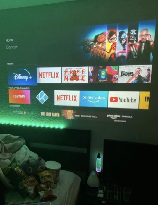 A reviewer shows the movie projector in use on an indoor wall, displaying vibrant images.
