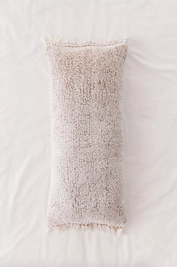 Photo of the beige body pillow on crisp white sheets