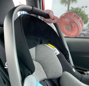 The pink fan with flexible clamps securing it to a car seat handle